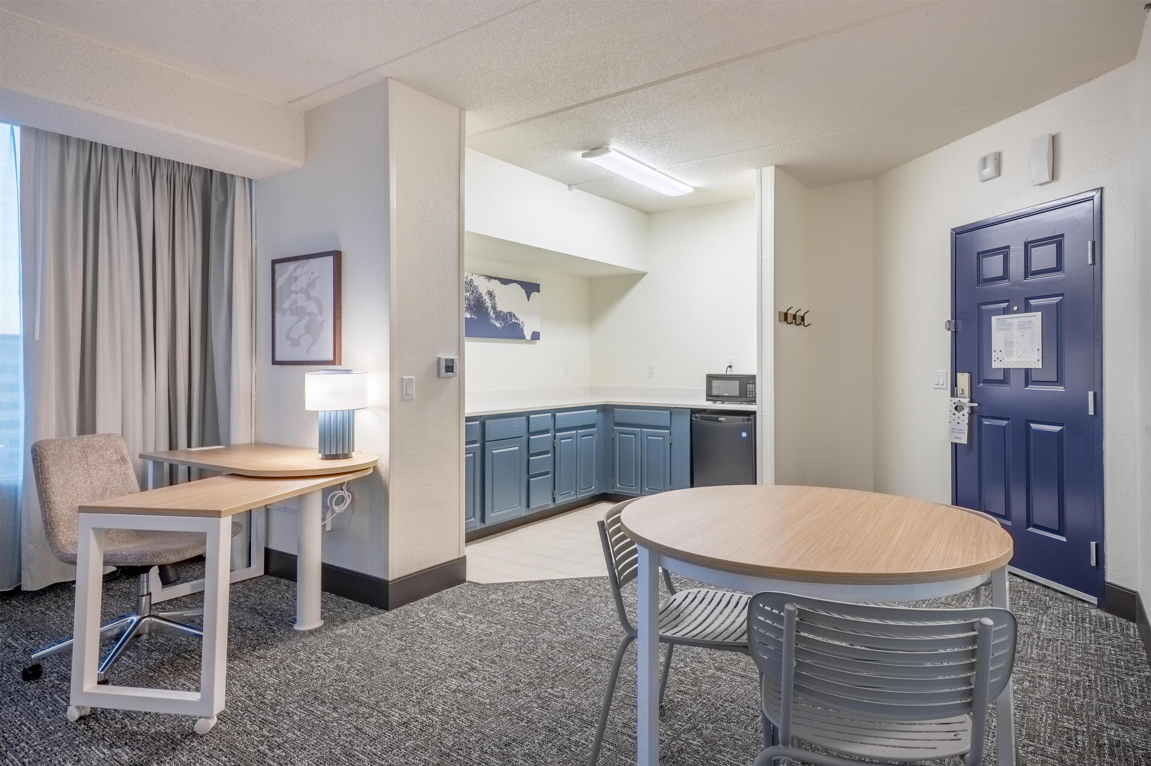 A hotel room with a dining area, a kitchenette, and a bathroom.