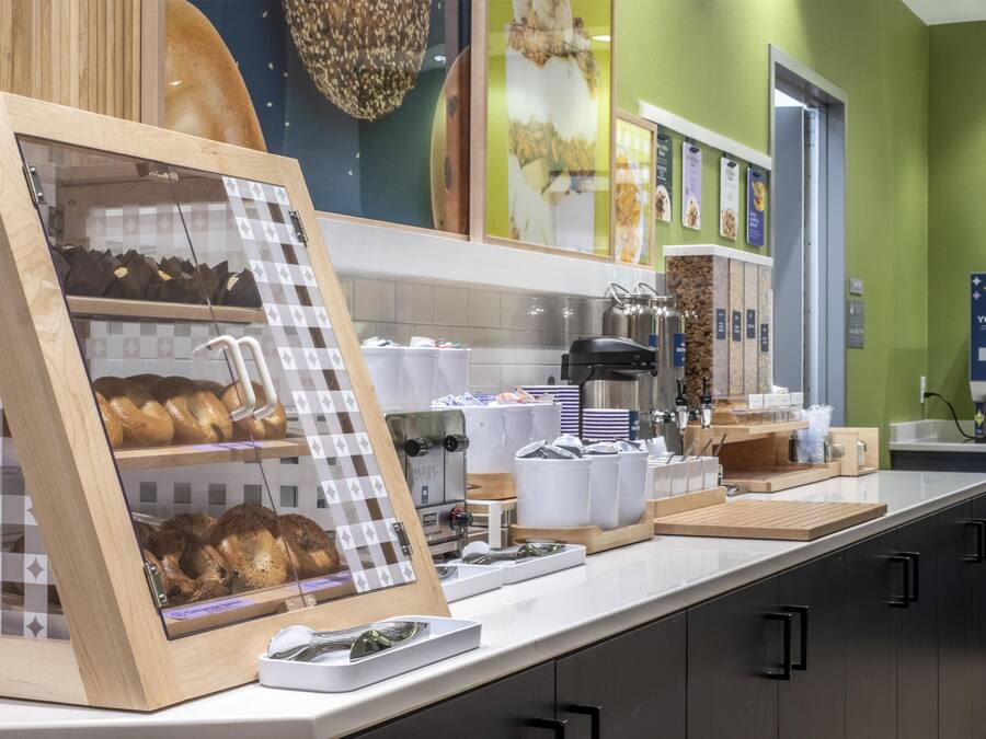 A bakery display with bread and pastries, a coffee machine, and a yogurt station in a cafe setting.