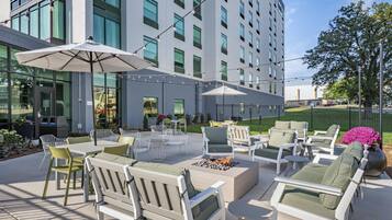 An outdoor seating area with tables, chairs, and umbrellas, surrounded by a modern building with large windows.