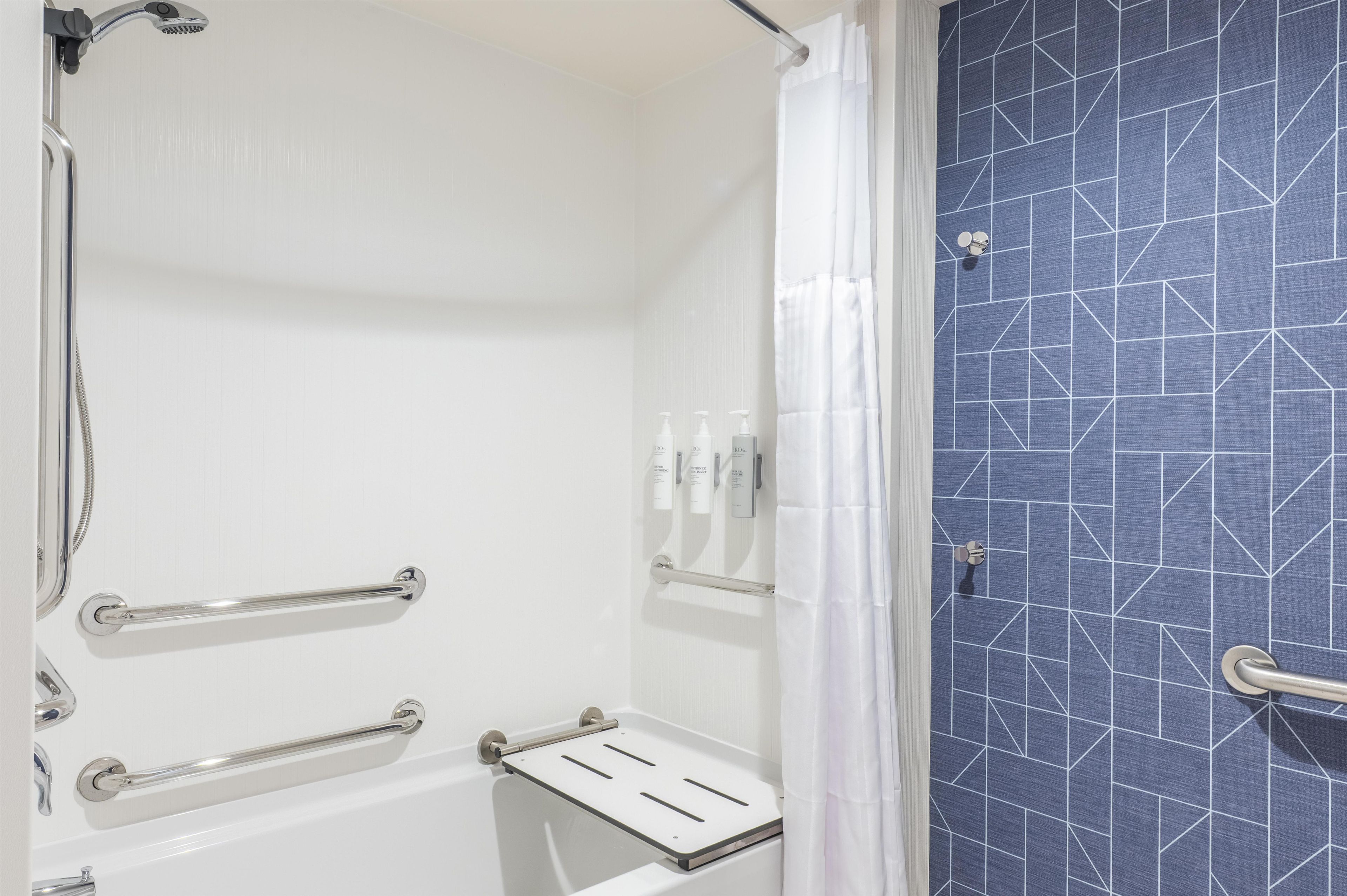 Une salle de bain avec une douche, des toilettes et un lavabo. Elle est équipée de barres d'appui et d'un porte-serviettes.