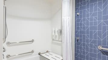 Un baño con ducha, bañera y retrete. Hay barras de apoyo y un perchero para toallas.