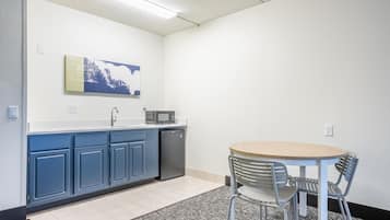 Una pequeña kitchenette con microondas, pileta y armarios. Hay una mesa redonda con dos sillas y una alfombra en el suelo.