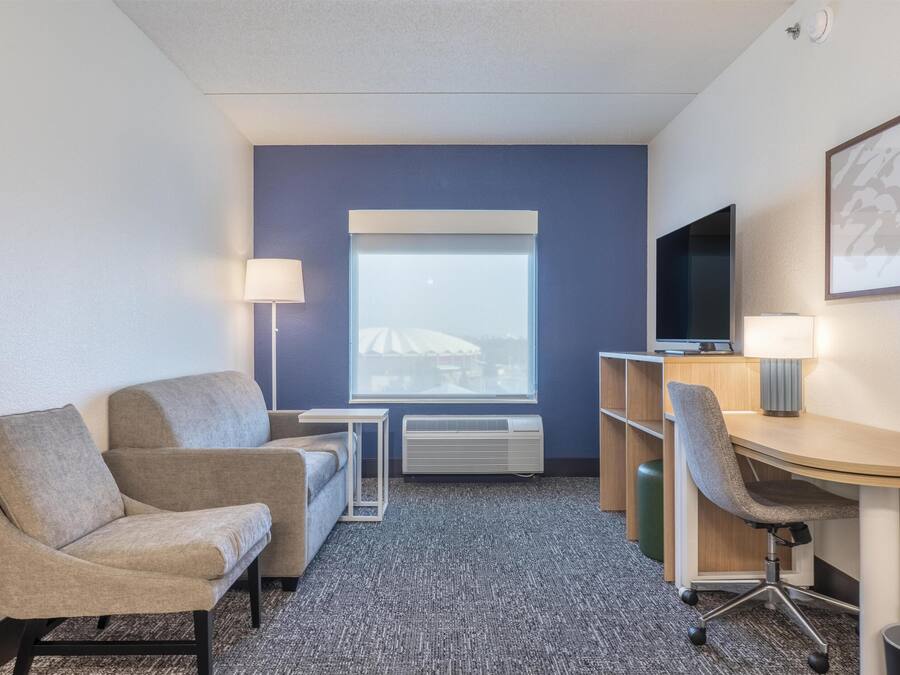 Une chambre d’hôtel équipée d’un canapé, d’un bureau avec une chaise, d’une télévision, d’une lampe et d’une fenêtre donnant sur un immeuble.