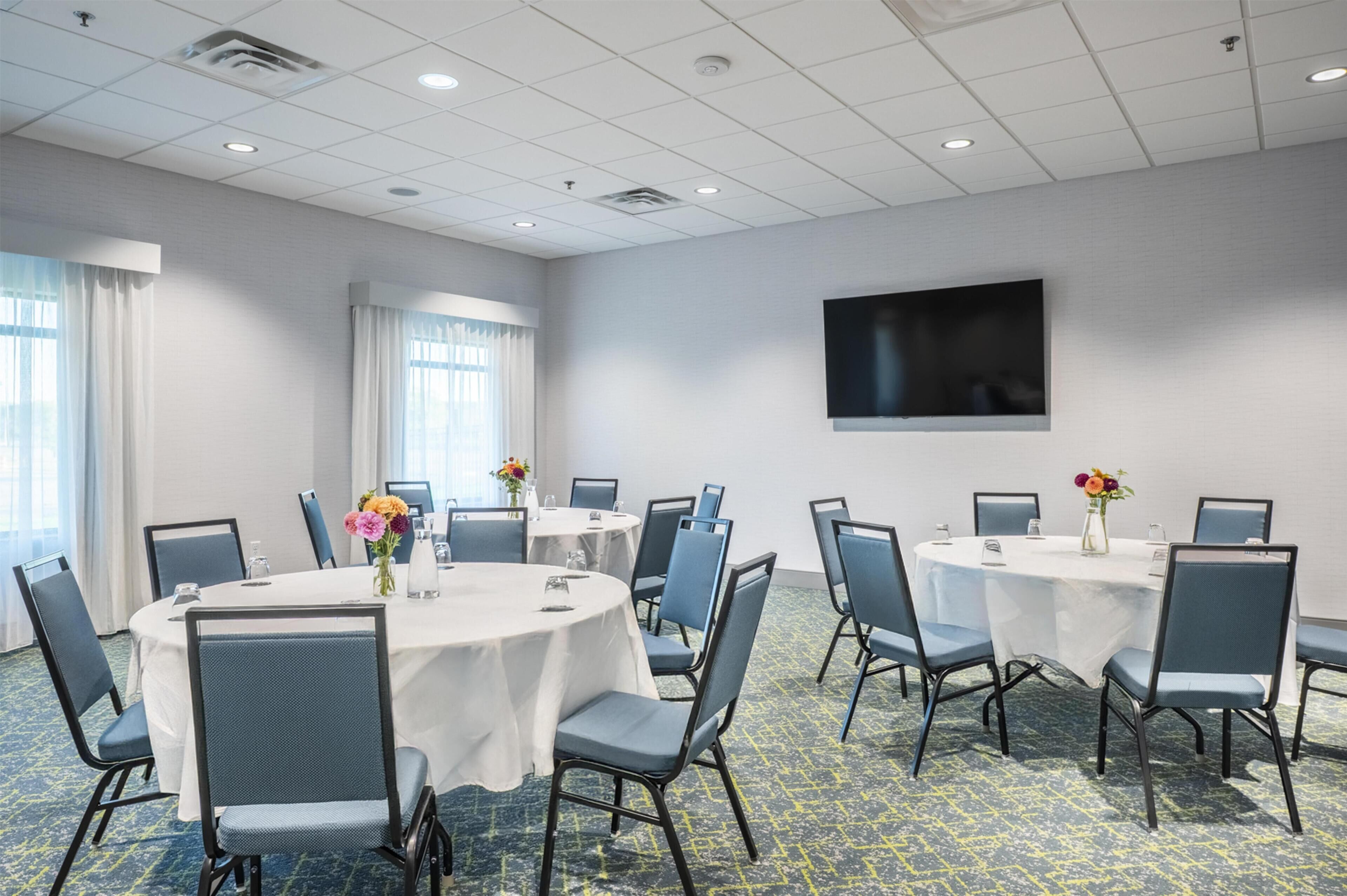 A conference room with round tables, chairs, and a flat-screen TV on the wall.