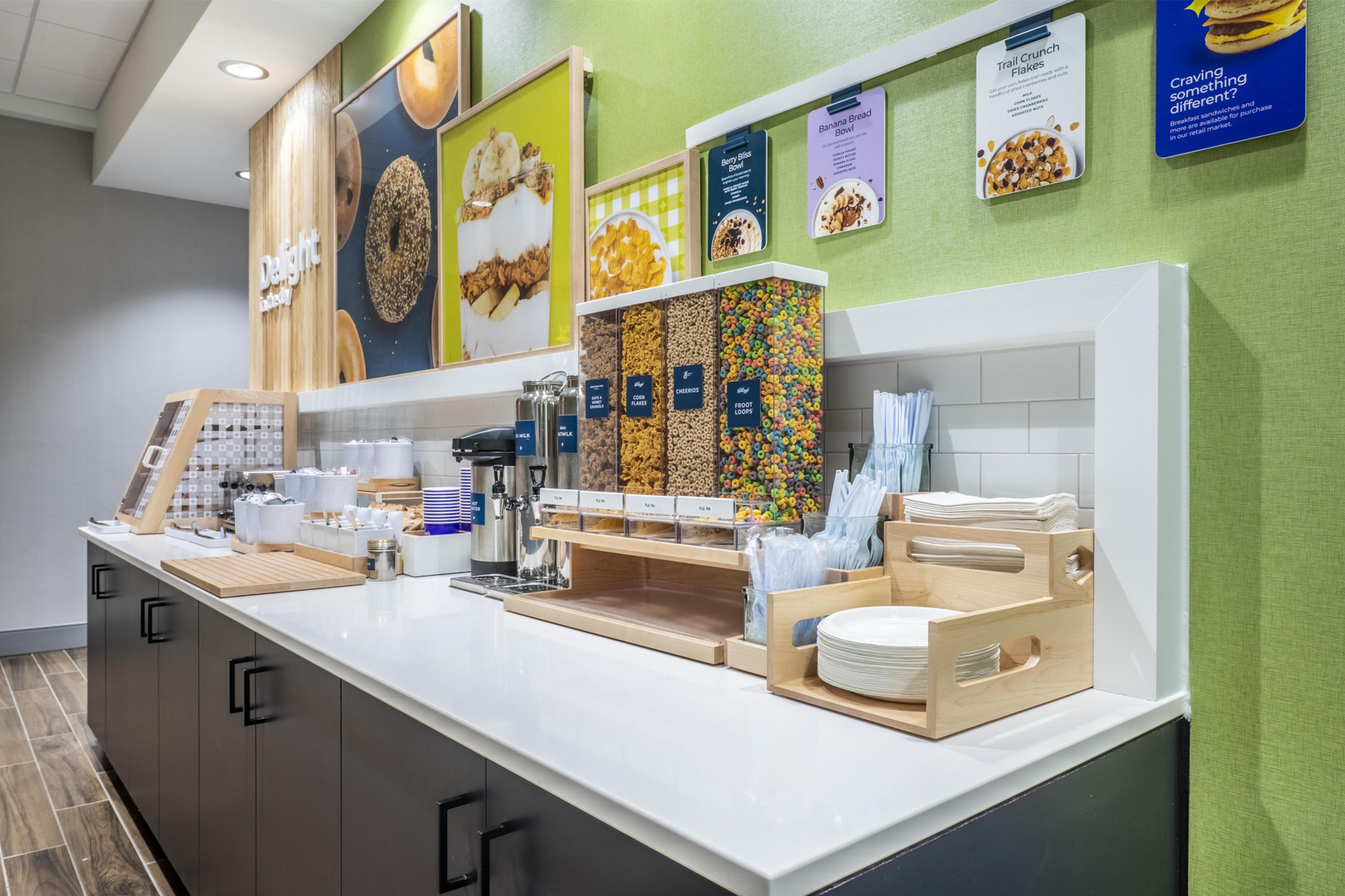 A breakfast buffet counter with various food options, including cereal and granola bars, and a coffee station.