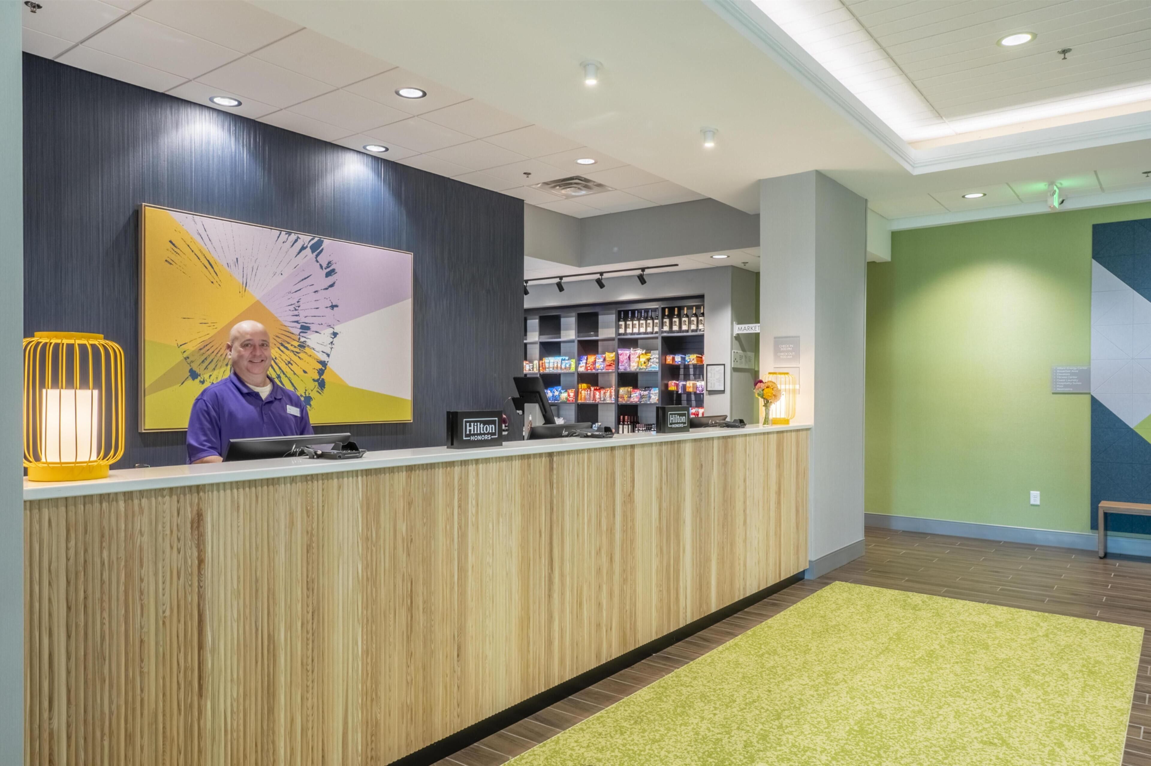 Zona de recepción de un hotel con un mostrador de madera, un cuadro abstracto grande y un minibar.
