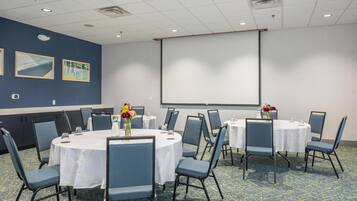 A conference room with round tables, blue chairs, and a projector screen on the wall.