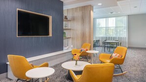 Un'area lounge moderna con poltrone gialle, un'ampia televisione a schermo piatto e vista all'esterno tramite ampie finestre.