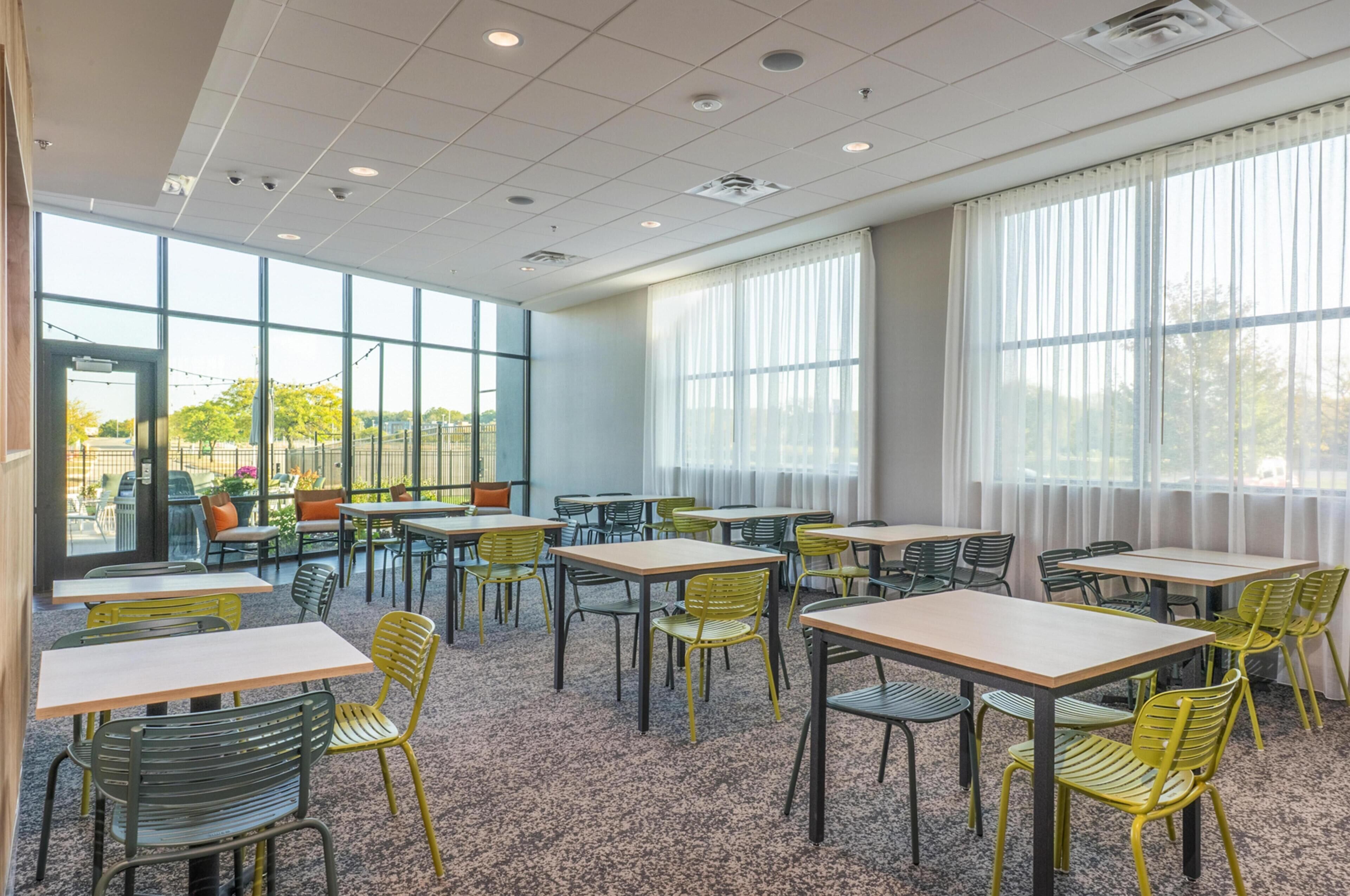 A modern indoor dining area with tables and chairs, large windows, and a view of the outdoors.