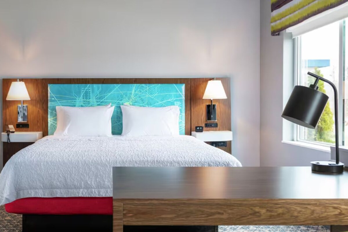 Une chambre d’hôtel avec un lit, deux lampes de chevet, une table de chevet, une fenêtre et un miroir.