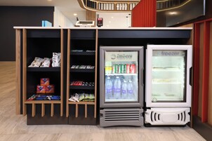 Zona de máquinas expendedoras con dispensador de bebidas, un congelador y estantes llenos de refrigerios y bebidas.