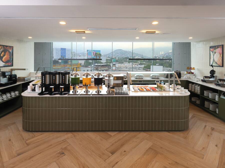 Un café moderne avec un comptoir central, différents types de machines à café et une vue sur le paysage urbain grâce à de grandes fenêtres.