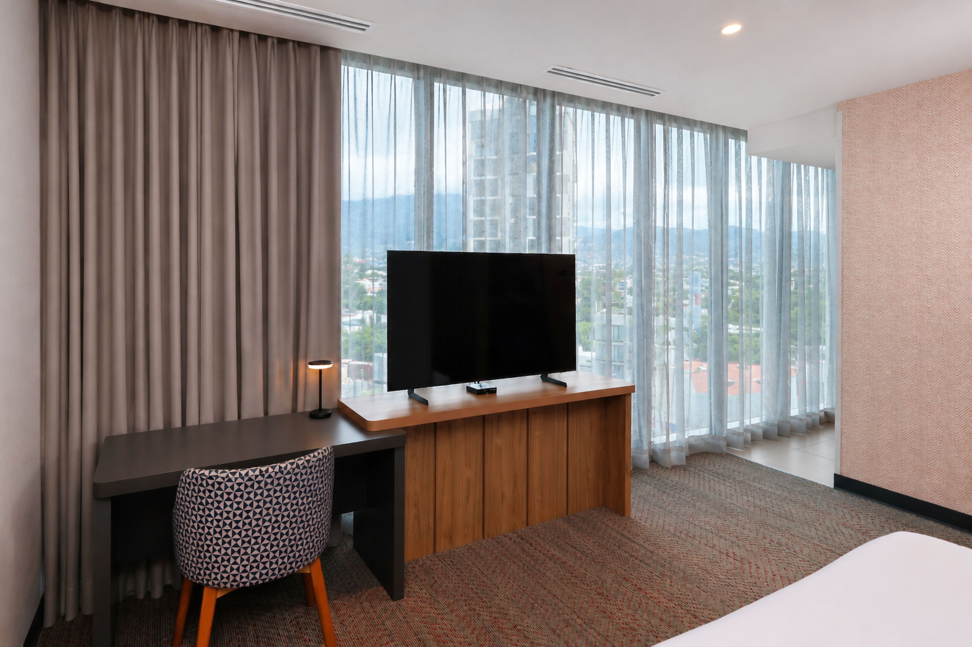 Een hotelkamer met een groot raam, een bureau met een televisie, een stoel en een bed.