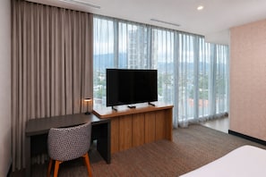 Una habitación de hotel con un ventanal grande, un escritorio con televisor, una silla y una cama.