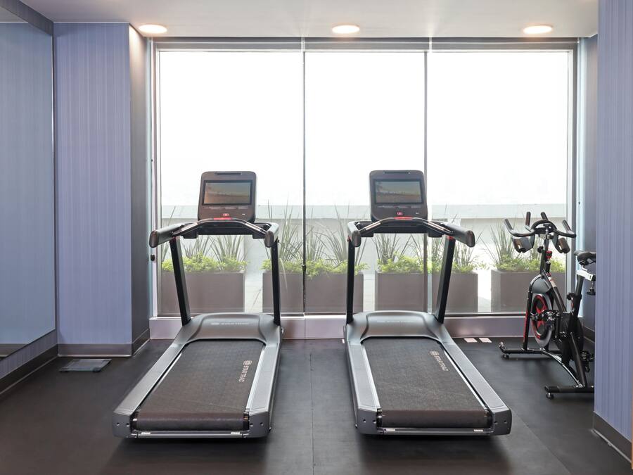 A gym with treadmills and an exercise bike, large windows, and a view of greenery.