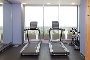 Un gimnasio con cintas de correr y una bicicleta estática, ventanas amplias y vistas a zonas verdes.