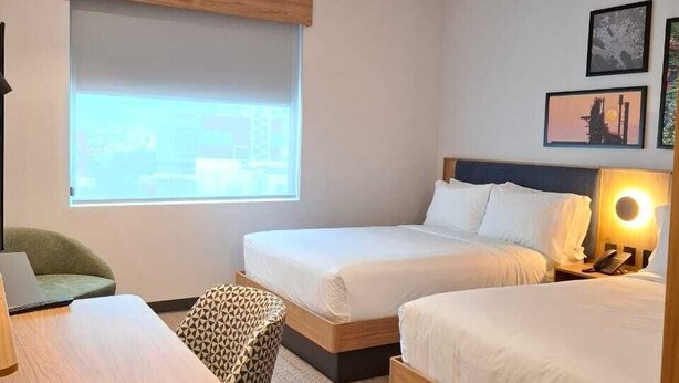 Ein Hotelzimmer mit zwei Betten, einem Schreibtisch, einem Sessel, einem Fenster und einer Lampe.