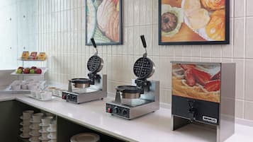 A breakfast buffet setup with waffle makers, a fruit display, and a wall-mounted food display.