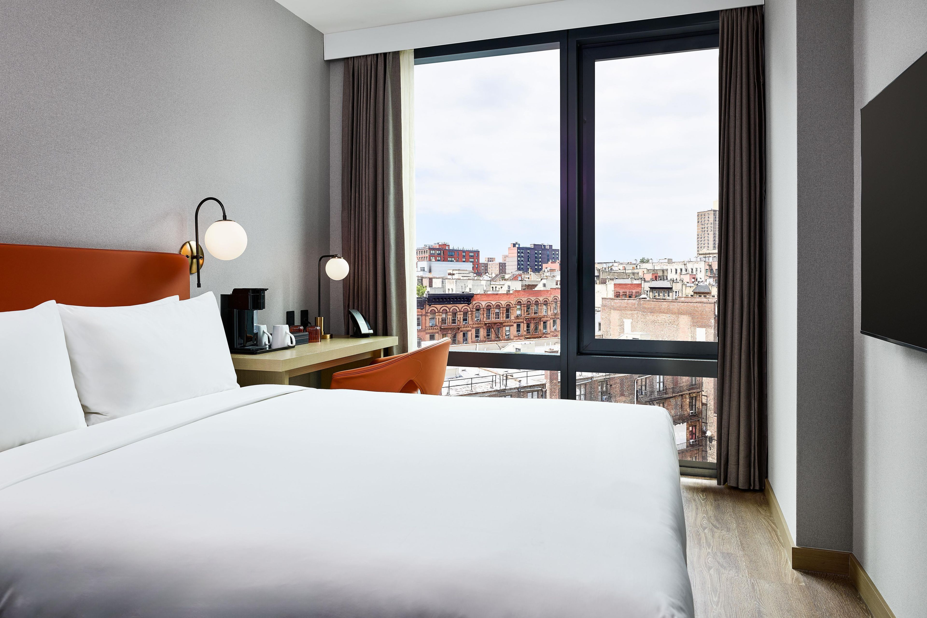 Une chambre d’hôtel avec un grand lit, un bureau, une chaise, une télévision et une vue sur la ville.