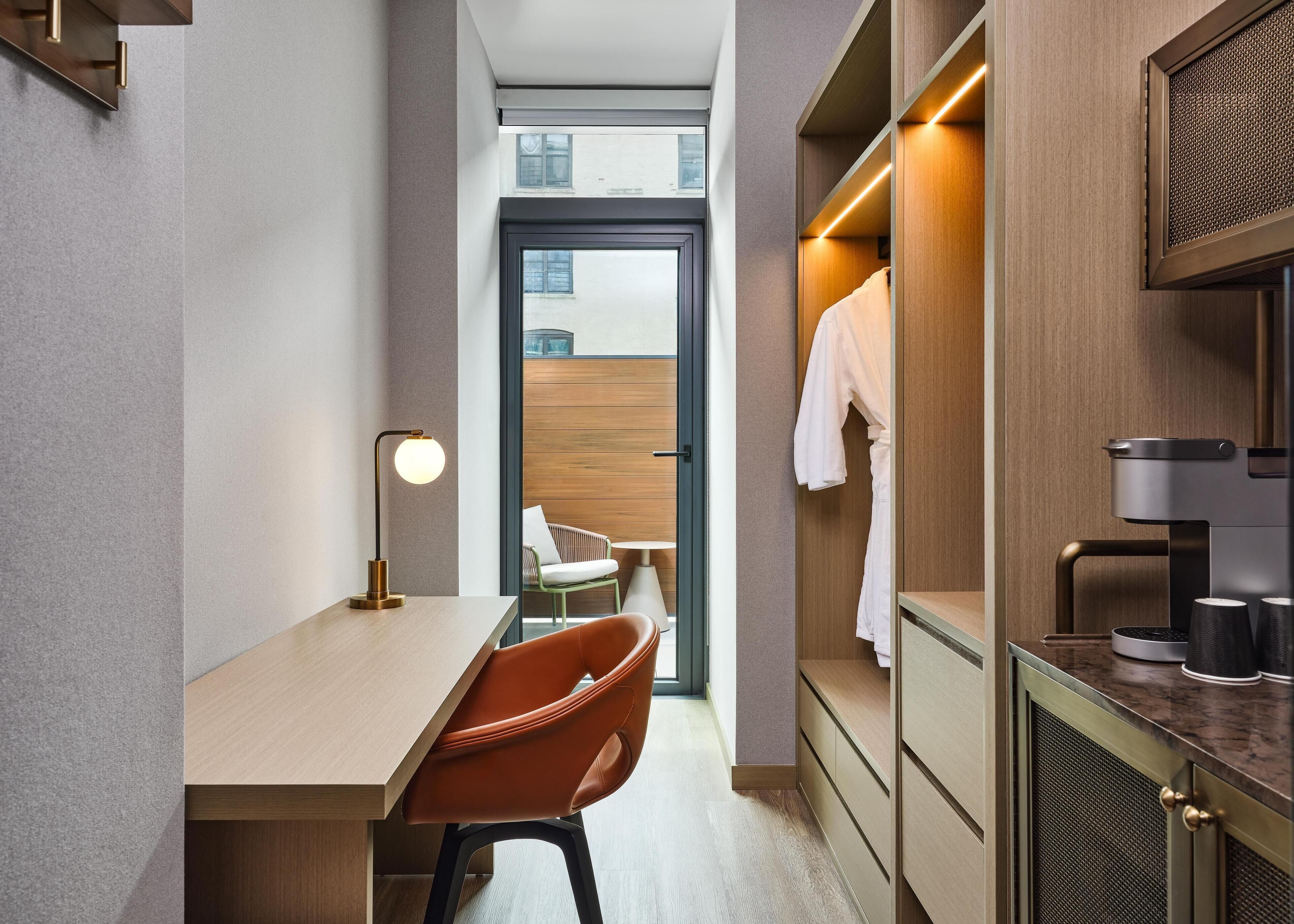 A modern hotel room with a desk, chair, and a view of the city through a large window.