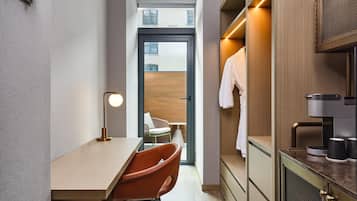 A modern hotel room with a desk, chair, and a view of the city through a large window.