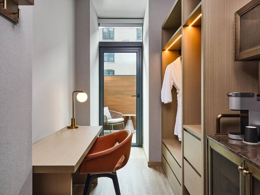 A modern hotel room with a desk, chair, and a view of the city through a large window.