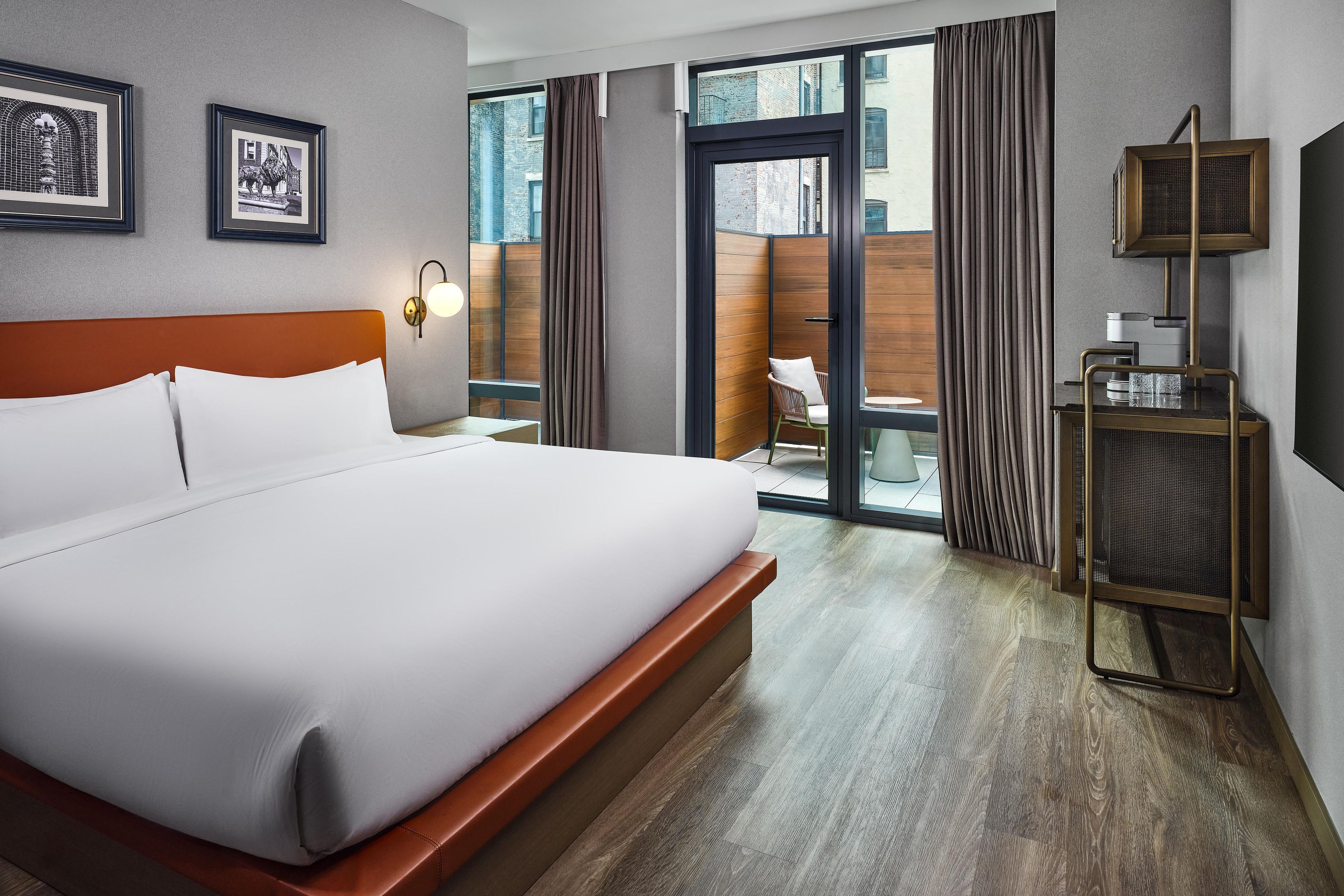 A hotel room with a large bed, a desk with a lamp, a window with curtains, and a view of the outside.