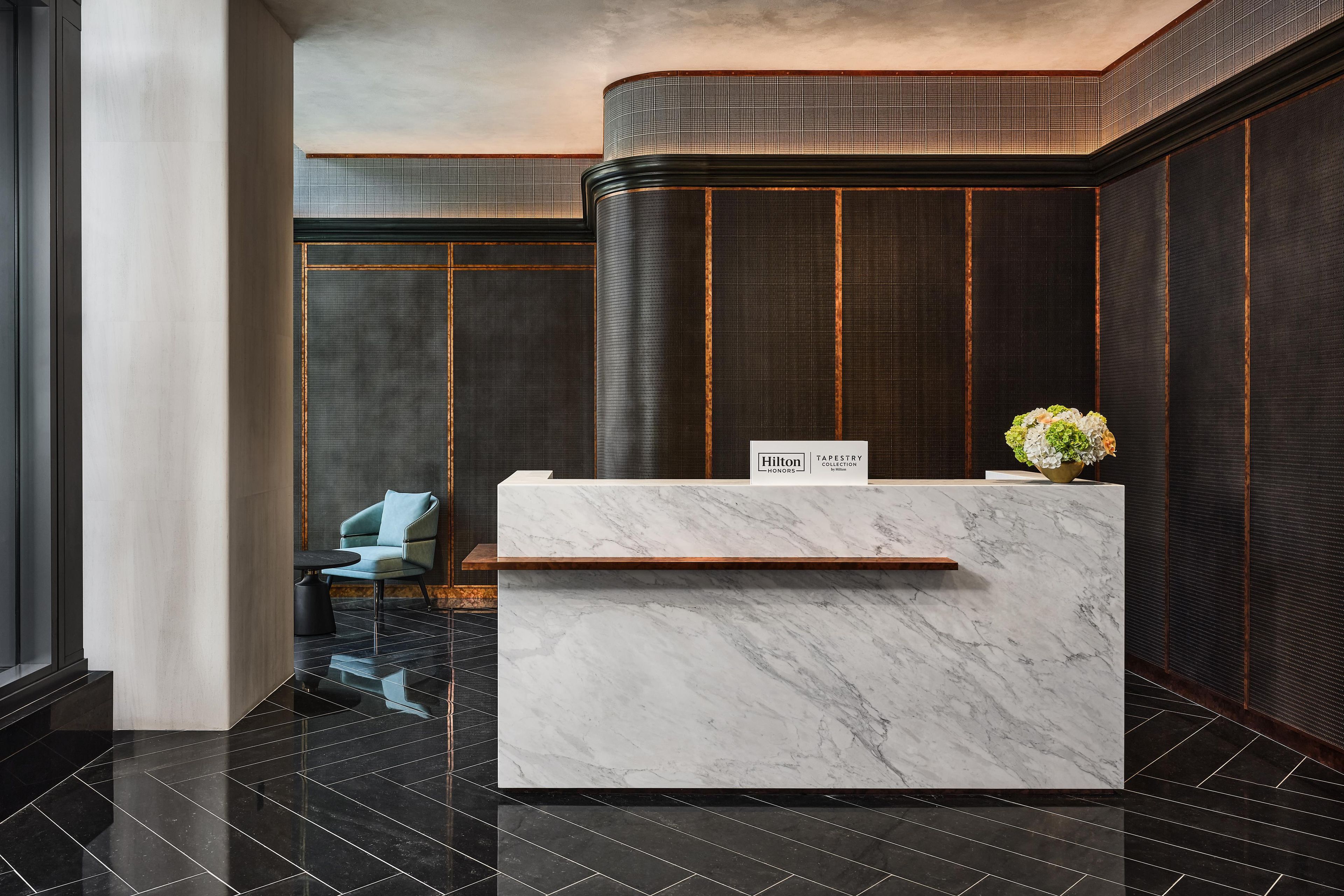 Un mostrador de recepción de hotel con encimera de mármol, un cartel que indica 'Hilton Honors' y una silla a la izquierda.