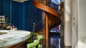 Un interior modern amb una escala espiraltra, un taulell de marbre i cadires verdes.