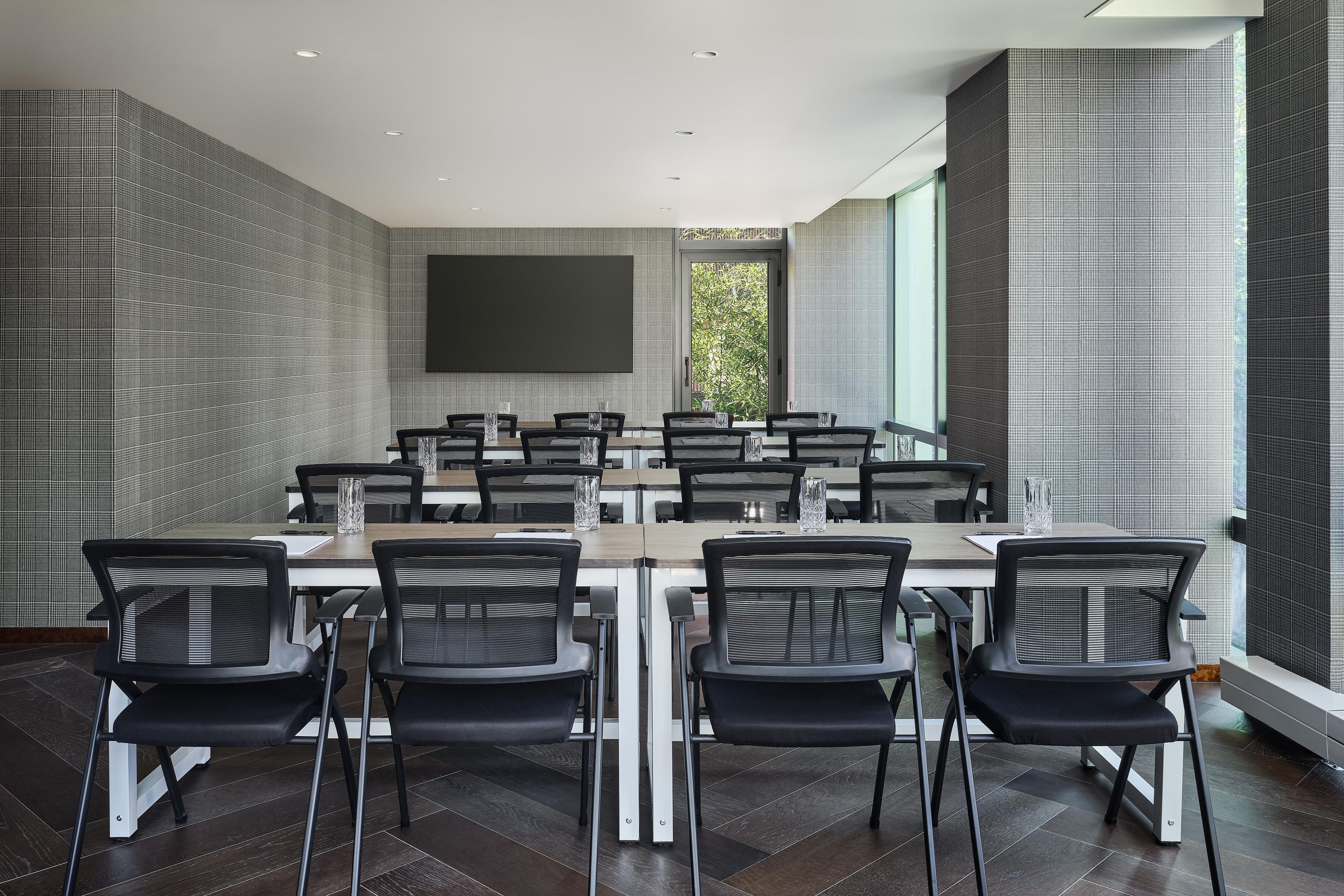 A modern conference room with a large table, black chairs, and a large screen.