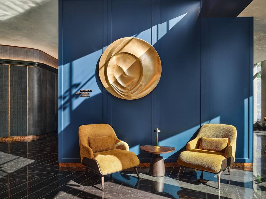Un vestíbulo moderno con dos sillones, una mesa redonda y una gran pieza decorativa en la pared.