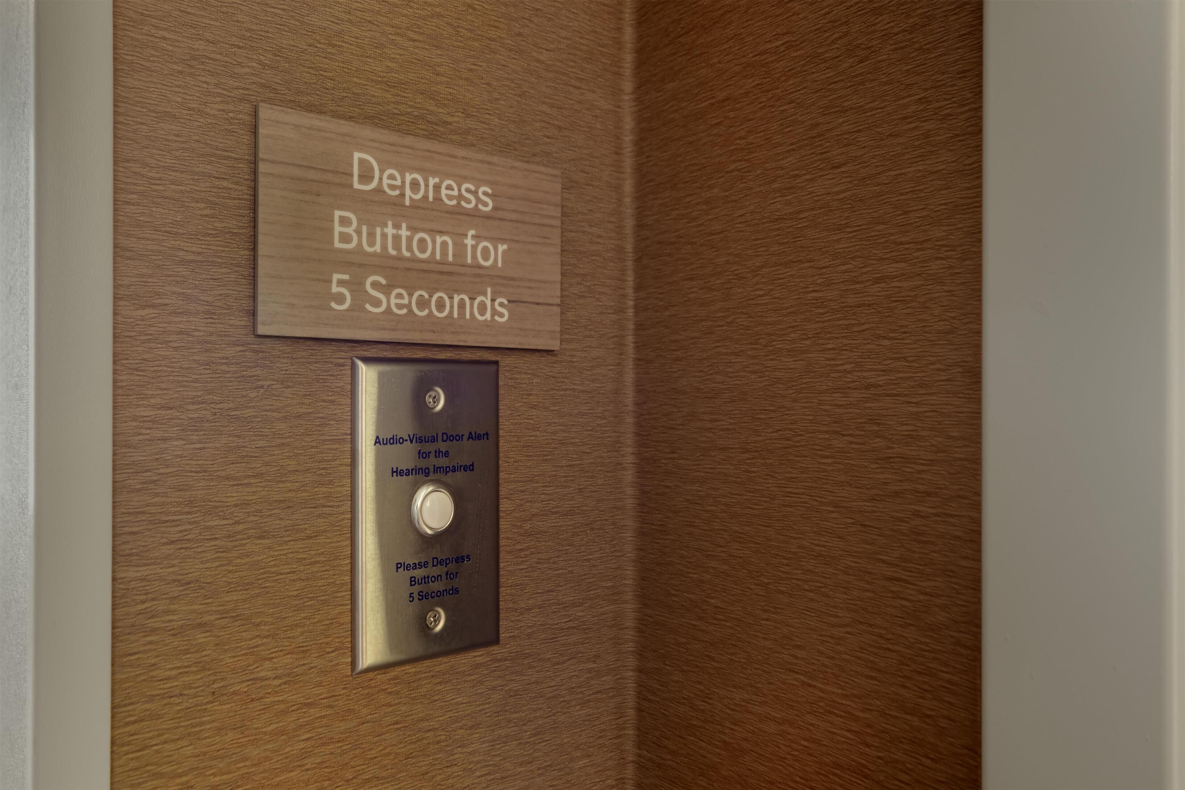 Une porte en bois munie d’un bouton poussoir et d’une indication invitant à appuyer sur le bouton pendant 5 secondes.