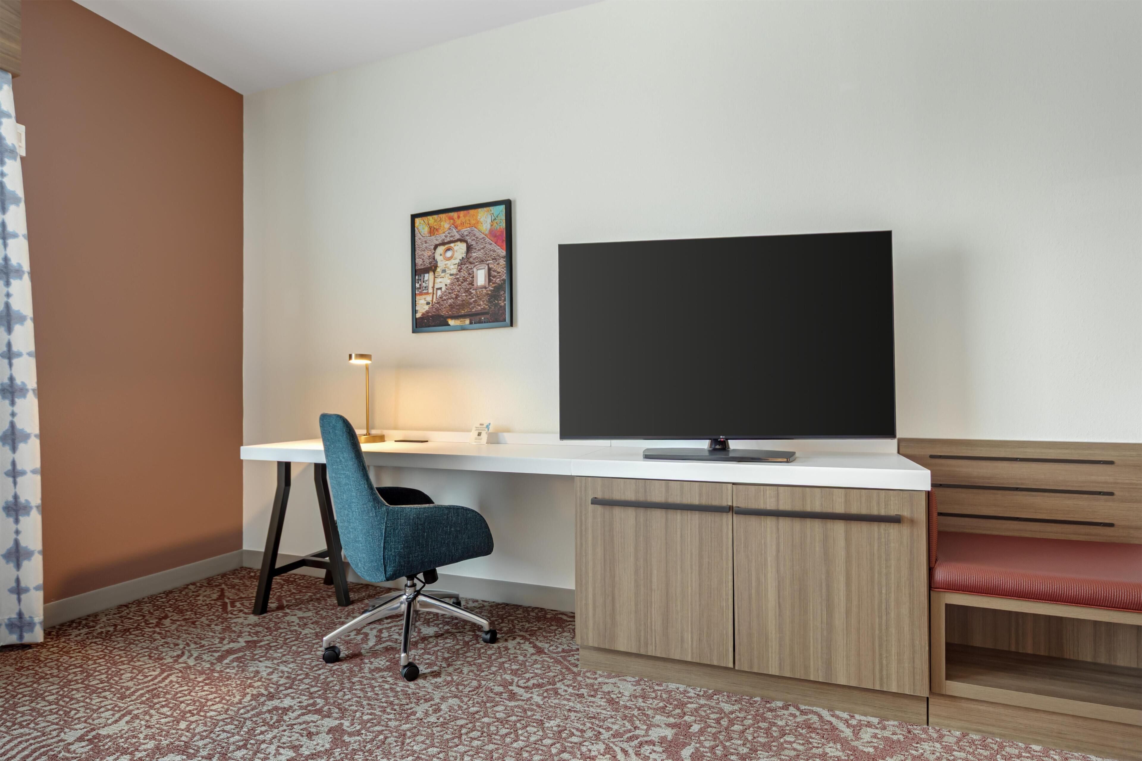 Una camera d'albergo con scrivania, sedia, televisione e una panca.