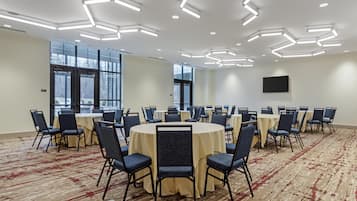Een vergaderzaal met ronde tafels, stoelen en een vloerbedekking.