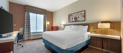 A hotel room with a bed, a desk, a chair, a television, a window with curtains, and a painting on the wall.