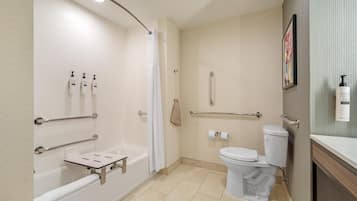 A bathroom with a bathtub, toilet, and shower. There are handrails, a towel rack, and a toilet paper holder.