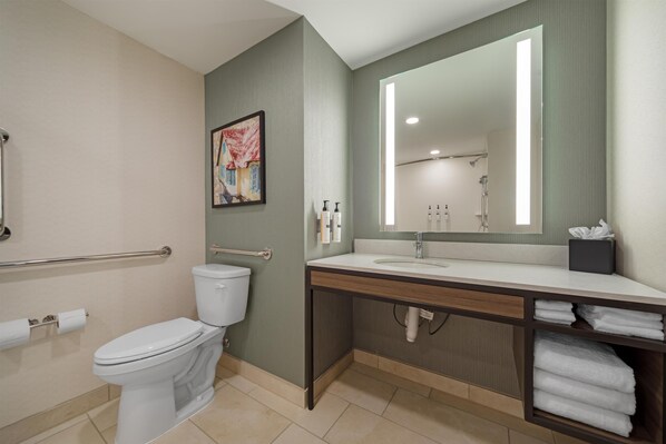 A bathroom with a toilet, sink, mirror, towel rack, and a handrail. - Hilton Garden Inn Media Philadelphia (Media)