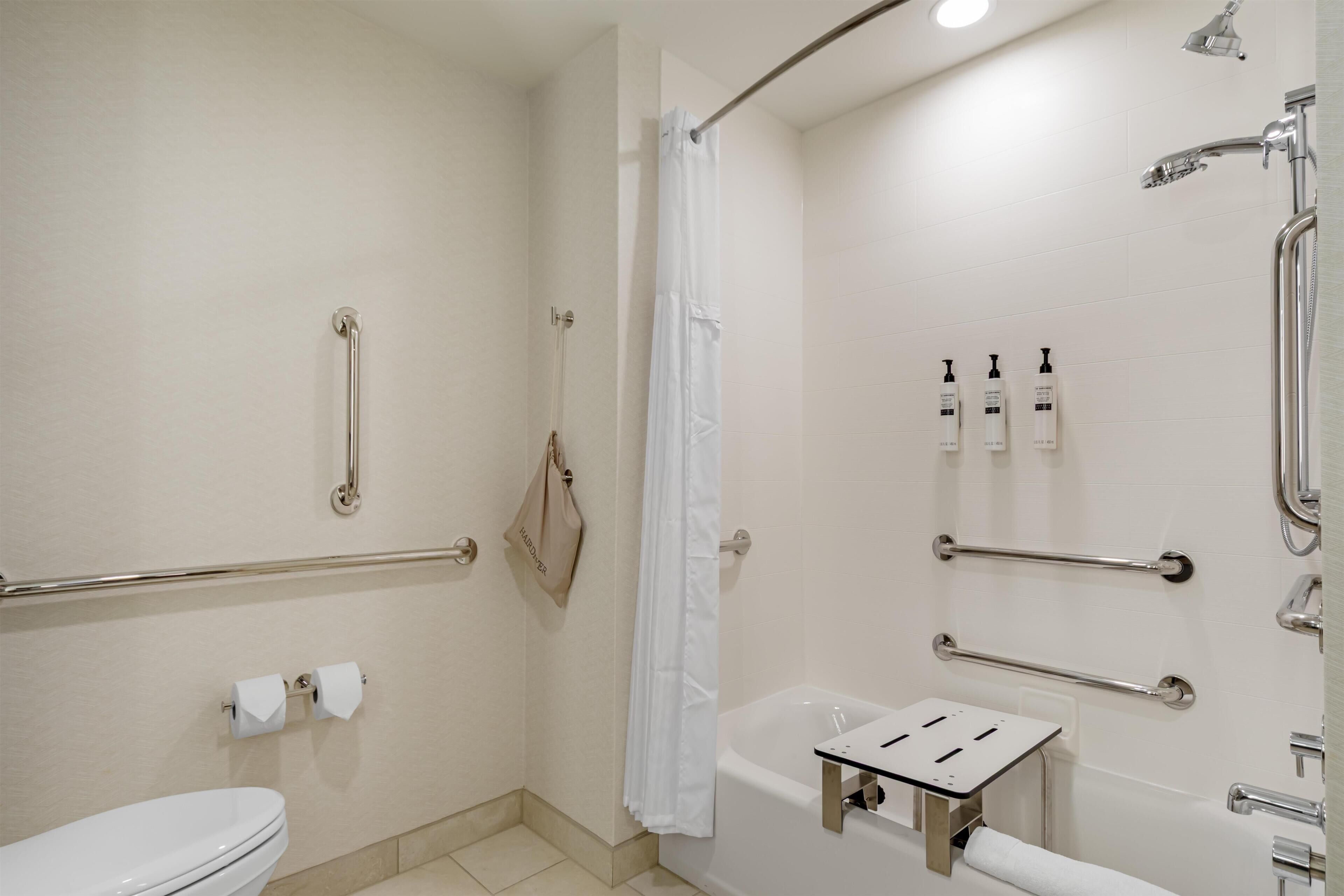 A bathroom with a toilet, a bathtub, a shower with a grab bar, and handrails.