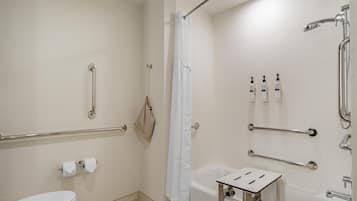 Un baño con inodoro, bañera, ducha con barra de apoyo y pasamanos.