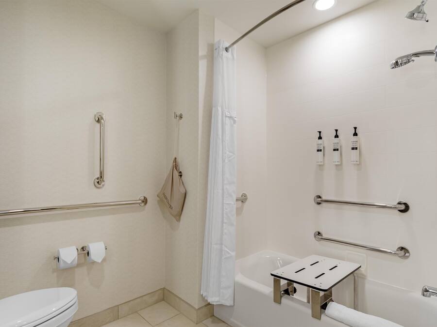 Un baño con inodoro, bañera, ducha con barra de apoyo y pasamanos.