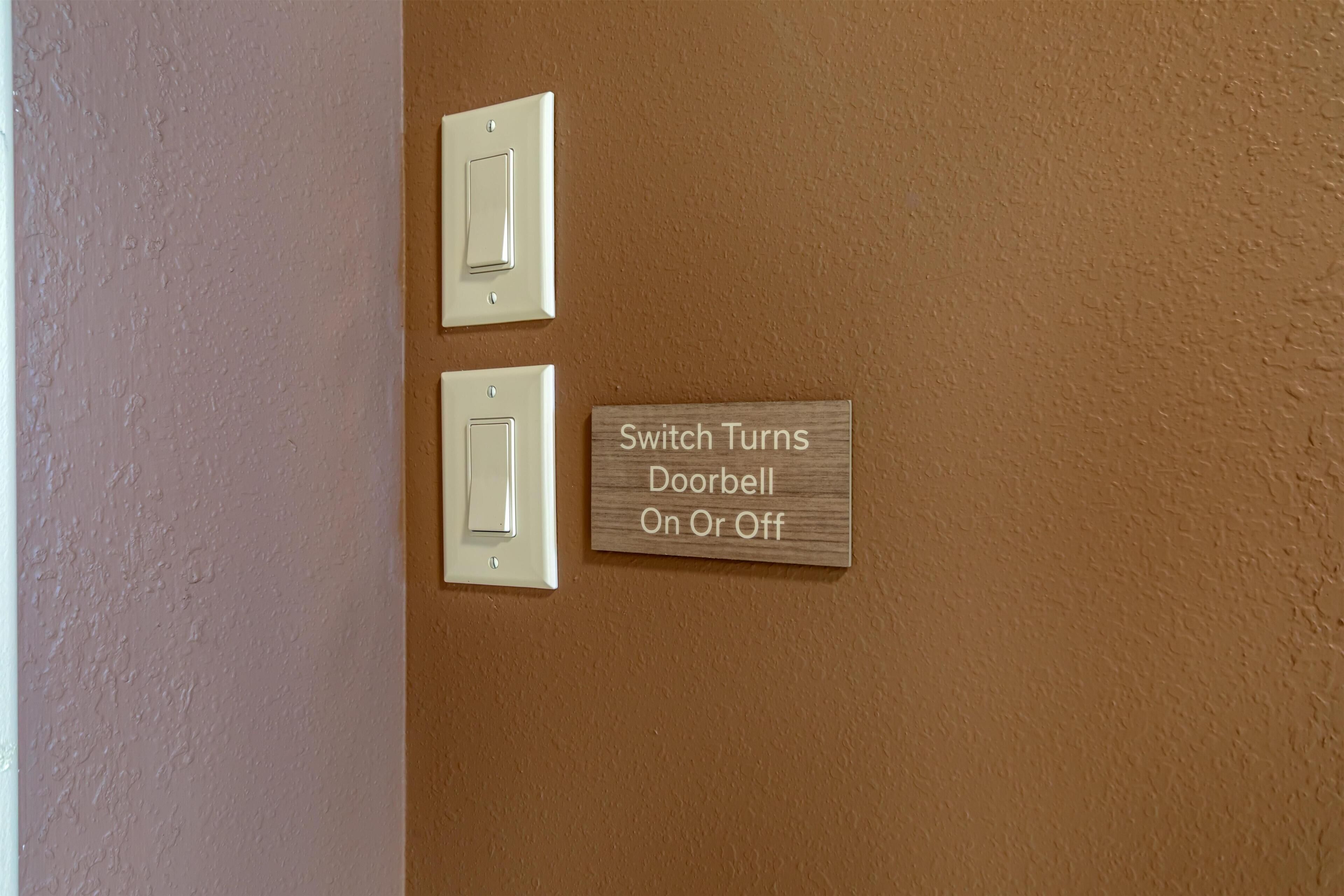 Two light switches and a wooden sign indicating the doorbell control.