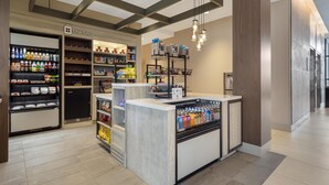 A modern retail space with a central counter, shelves stocked with products, and a sign reading 'The Shop.' - Hilton Garden Inn Media Philadelphia (Media)