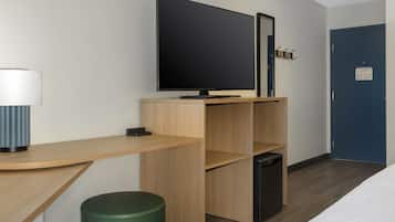 Une chambre d’hôtel moderne équipée d’une télévision à écran plat, d’un bureau avec une lampe, d’un pouf vert et d’une porte bleue.
