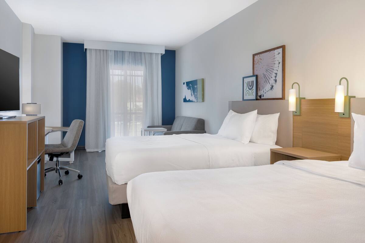 Ein Hotelzimmer mit zwei Betten, einem Schreibtisch, einem Stuhl und einem Fernseher.