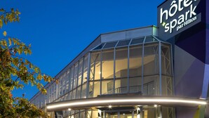 Een modern hotelgebouw met een glazen gevel, een opvallend bord met de tekst 'hotel spark par Hilton' en een goed verlichte ingang met treden die naar de deuren leiden.