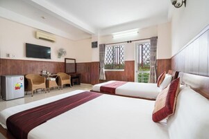 Quarto de hotel com duas camas, uma escrivaninha, uma cadeira, uma televisão e varanda com vista.
