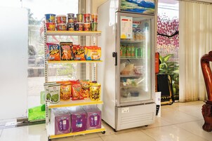 Máquina de vendas com lanches e bebidas, geladeira com cardápio e um vaso de planta.