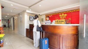Zona de recepción de un hotel con un mostrador de madera, un letrero rojo y dorado que indica la recepción, y una mujer de pie en el mostrador con una maleta.