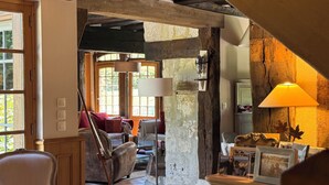 Ein rustikales Interieur mit freiliegenden Holzbalken, einem Fliesenboden, einer Couch, einem Sessel und einer Lampe.