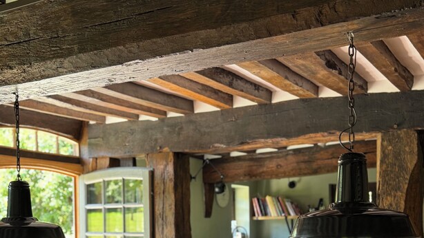 Eine rustikale Küche mit Holzbalken, einem Holztisch mit Äpfeln und hängenden Pendelleuchten.